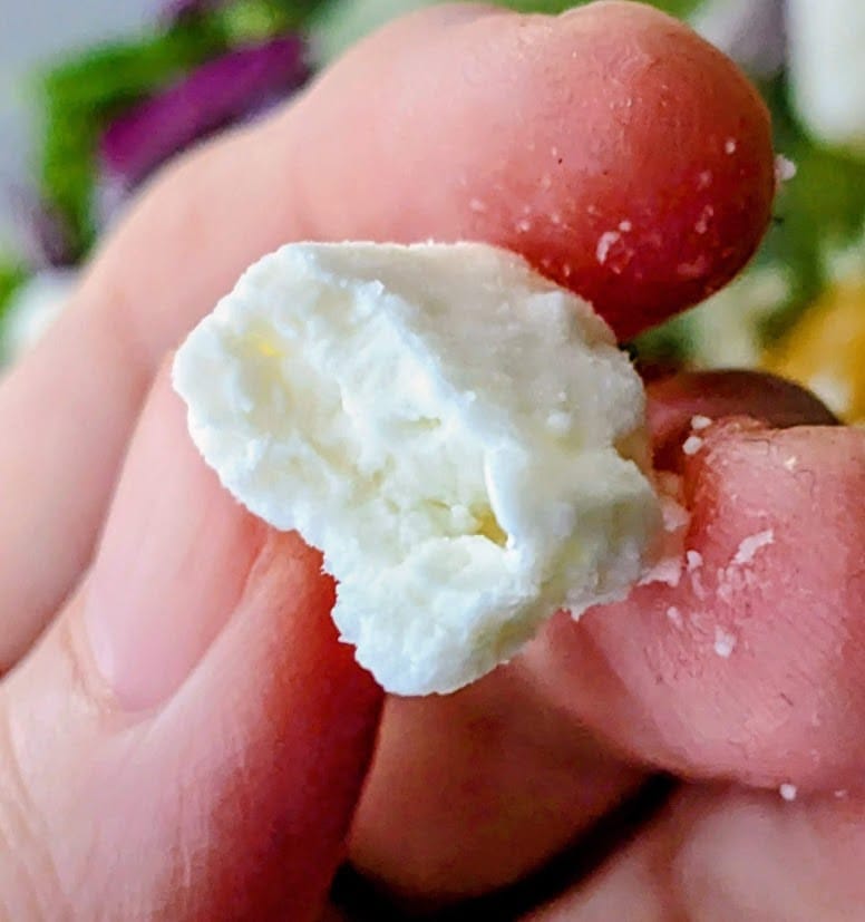 Fingers holding a chunk of feta cheese from President brand.
