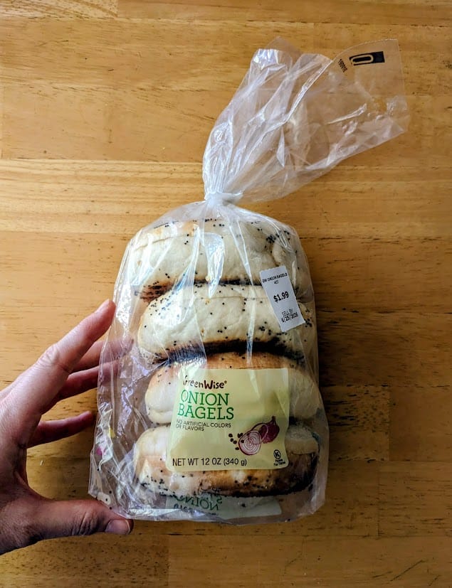 A hand holding a bag of four Onion Bagels from Publix Greenwise.
