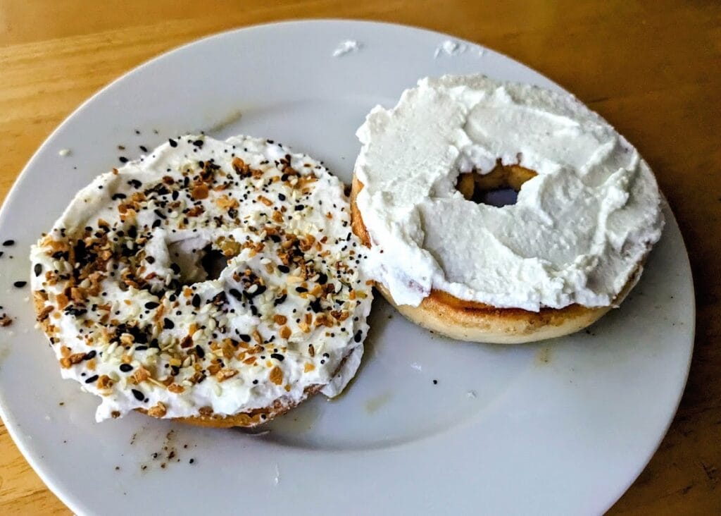 Two halves of a Publix Greenwise Onion Bagel topped with Greek yogurt and sprinkled with Aldi Everything seasoning.