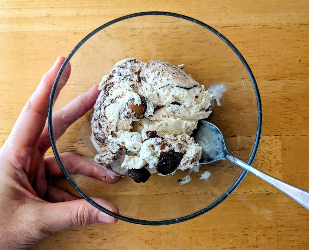 A hand holding a clear glass bowl of Buckeyes & Fudge peanut butter chocolate ice cream from Publix.
