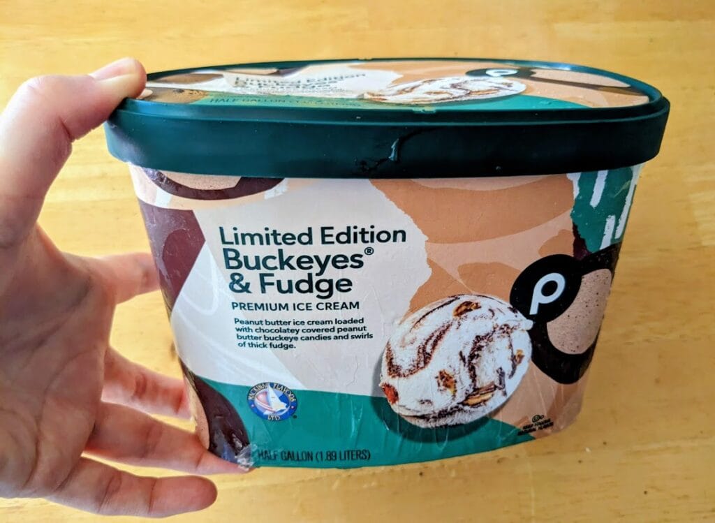 A hand holding a half-gallon carton of Publix Limited Edition Buckeyes & Fudge Premium Ice Cream.