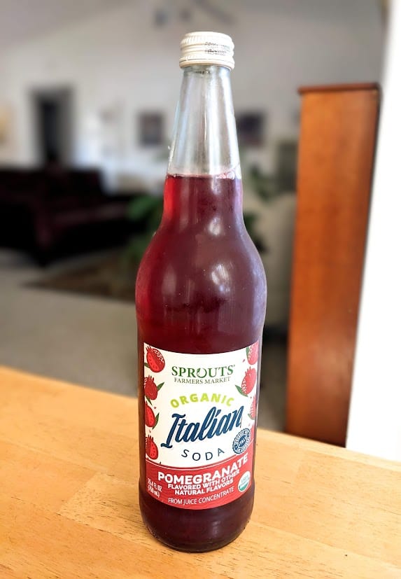 A tall glass bottle of Sprouts Organic Italian Soda Pomegranate flavor.