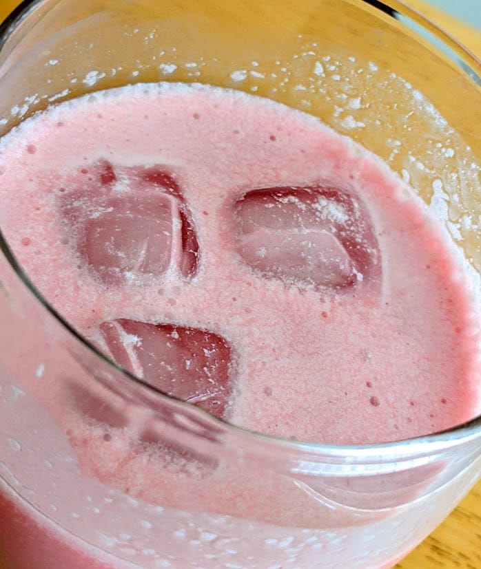 Close up of a glass of pomegranate cream soda with ice cubes.