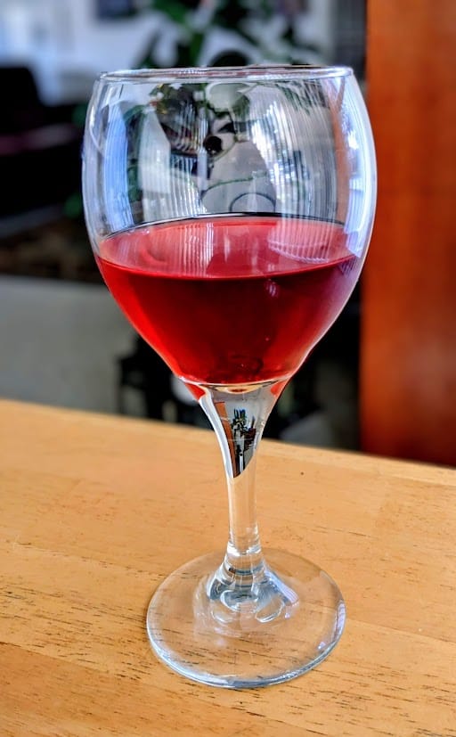 A clear wine glass with red Pomegranate Italian Soda from Sprouts Farmers Market.