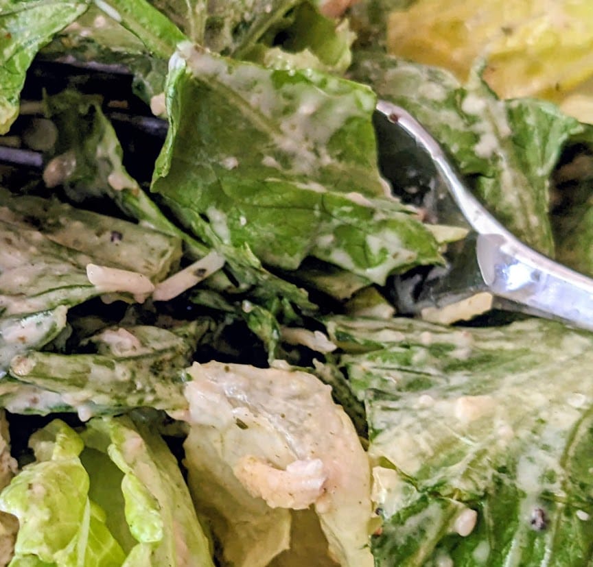 A fork in a pile of romaine lettuce coated in caesar dressing from a Taylor Farms salad kit.