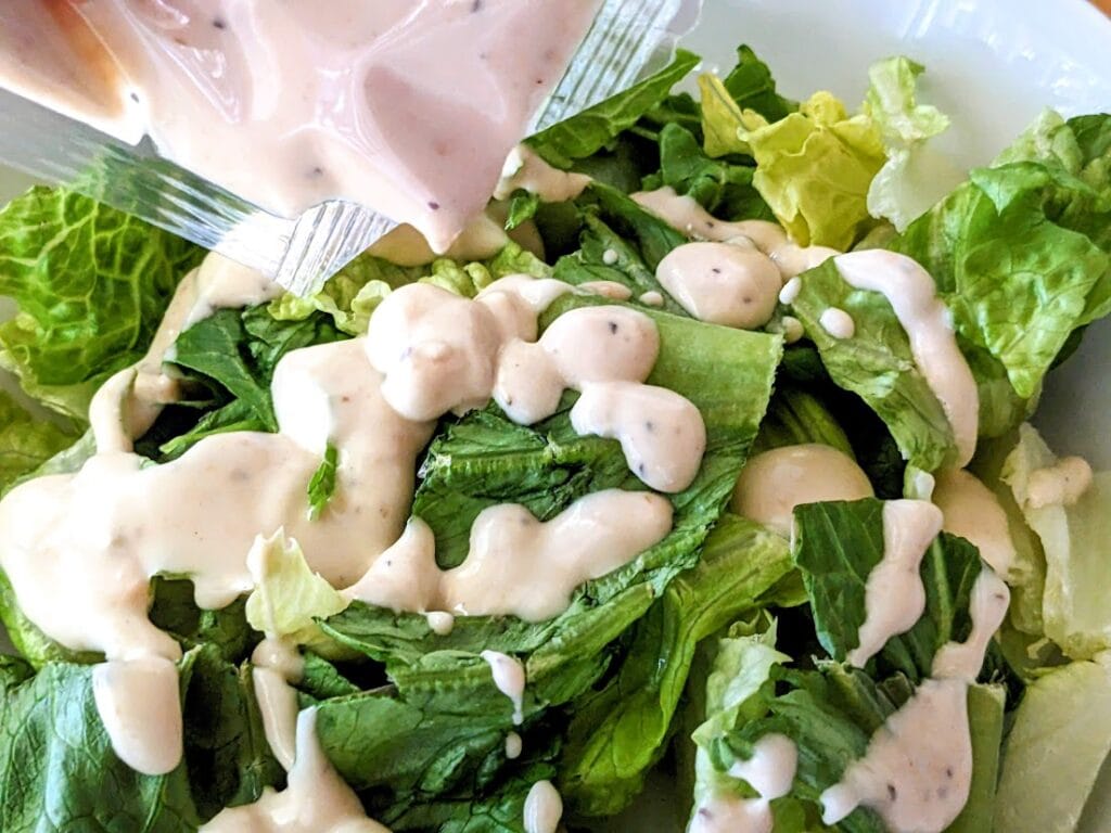 Caesar salad dressing being squeezed over romaine lettuce from a Taylor Farms salad kit.