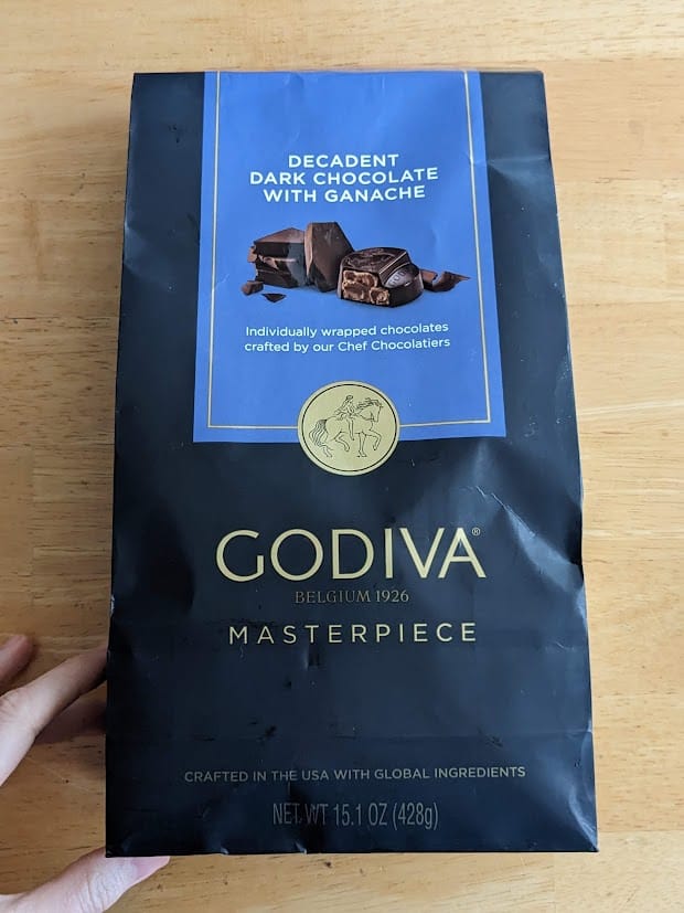 A hand holding a bag of Godiva Masterpiece Decadent Dark Chocolate Ganache candies from Costco.