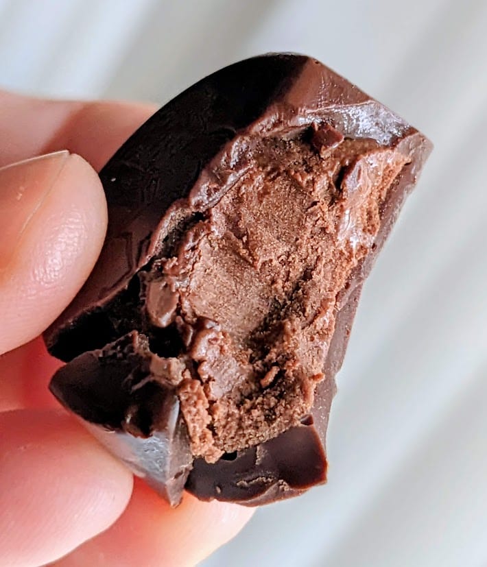 Fingers holding a bitten Godiva Masterpiece Ganache Chocolate, showing the filling.