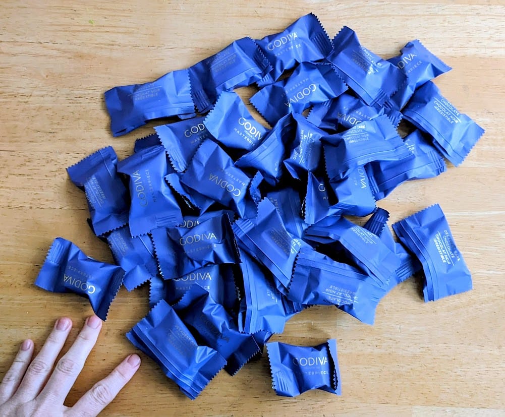 A hand next to a pile of purple-wrapped chocolates from Godiva.