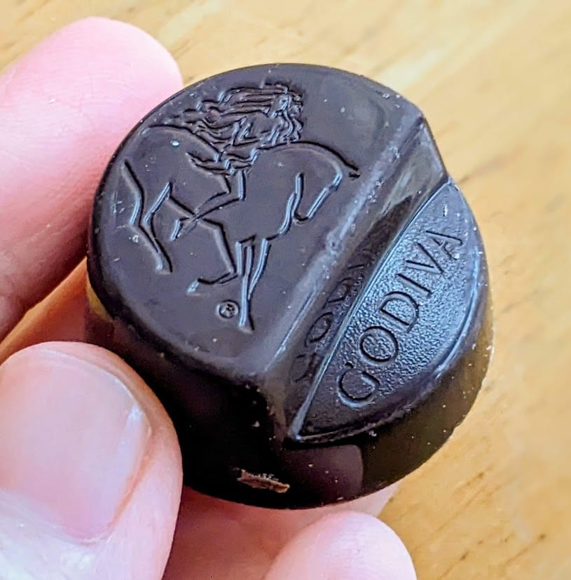 Fingers holding a whole Godiva Masterpiece Dark Chocolate Ganache.