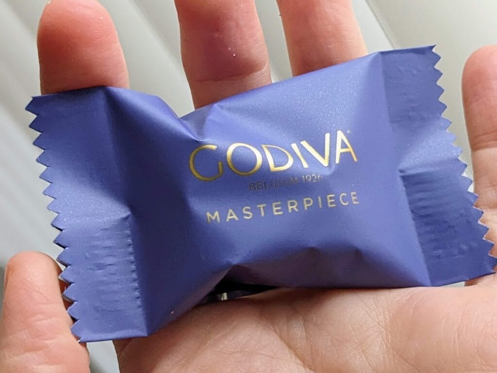 A hand holding a wrapped Godiva Masterpiece Ganache Chocolate.