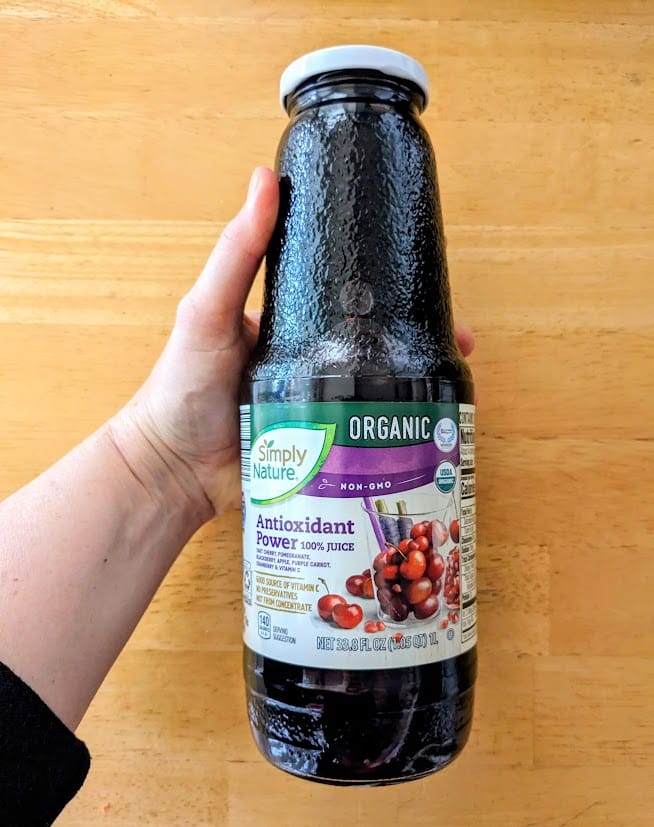 A hand holding a bottle of Aldi Antioxidant Power Organic Juice from Simply Nature brand.
