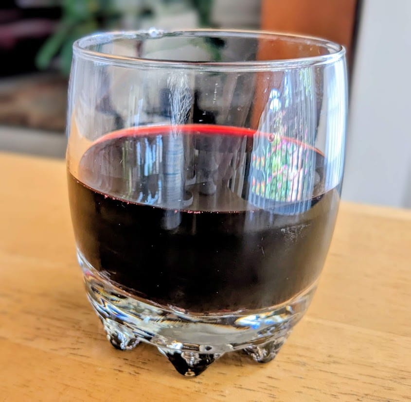 A clear glass with dark burgundy Antioxidant Power Organic Juice from Aldi's Simply Nature brand.