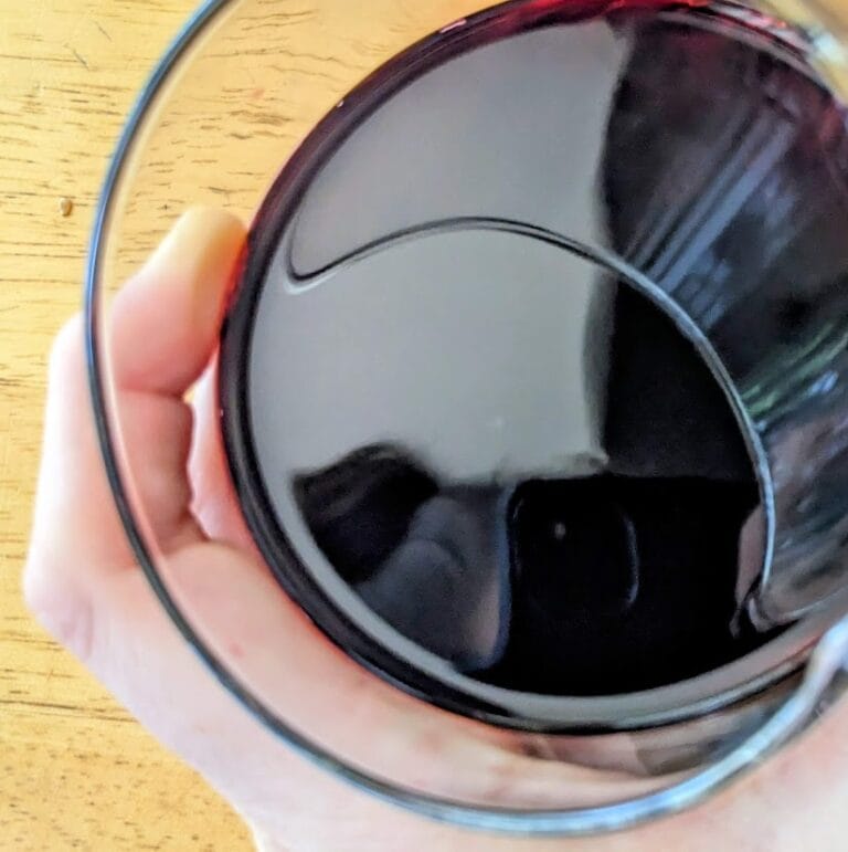A hand holding a glass filled with dark Antioxidant Power Organic Juice from Aldi.