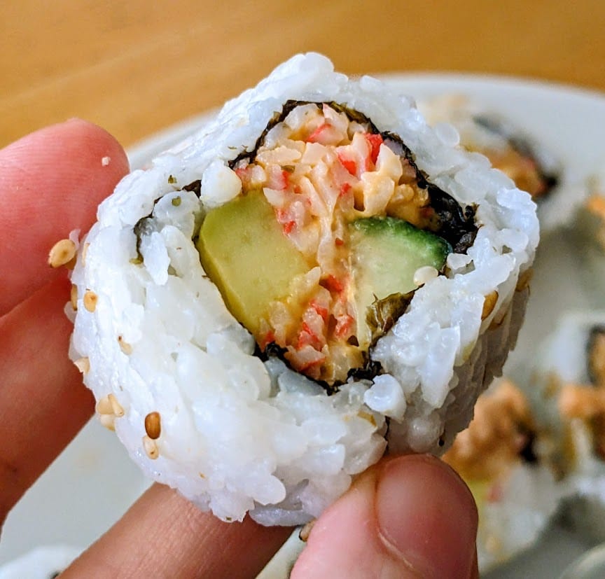 Fingers holding a piece of Costco California Crunch Combo Sushi, showing the avocado and cucumber.