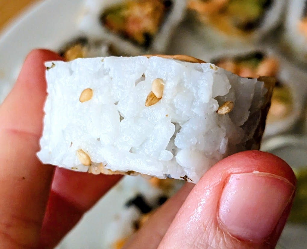 Fingers holding the side of a piece of Costco sushi, showing the sesame seeds.