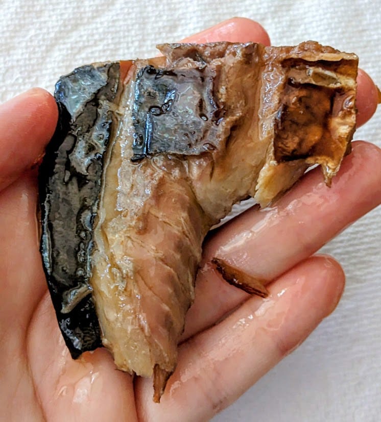 A hand holding a chunk of smoked mackerel from a can of Fishwife seafood.