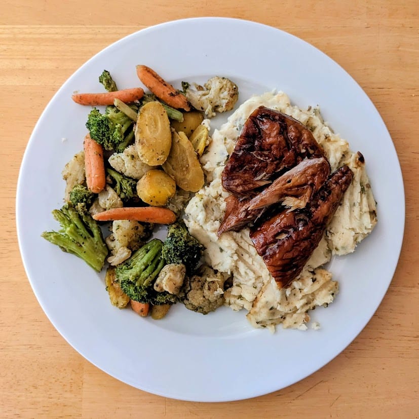 A white plate with vegetables, mashed potatoes, and Fishwife Smoked Mackerel with Chili Flakes.