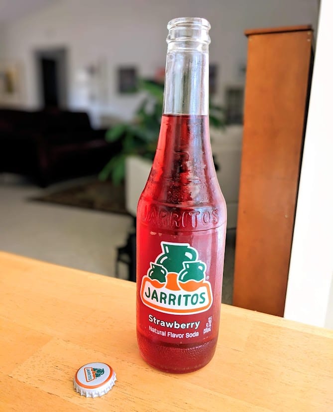 An open bottle of Jarritos Mexican Soda (strawberry flavor) on a kitchen table.