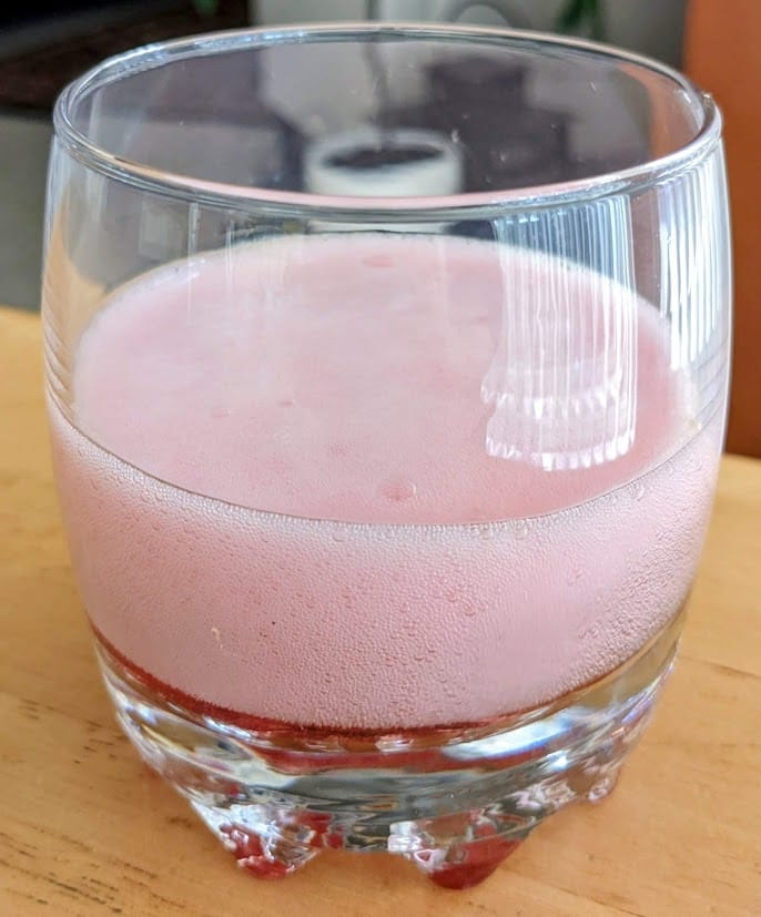 A glass with fizzy foam from Jarritos Strawberry Soda.