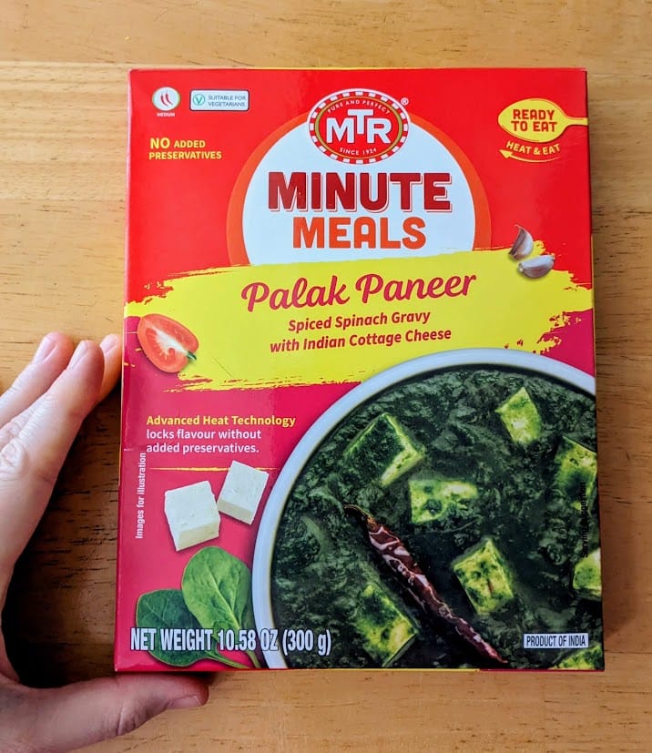 A hand holding a box of MTR Minute Meals Palak Paneer.