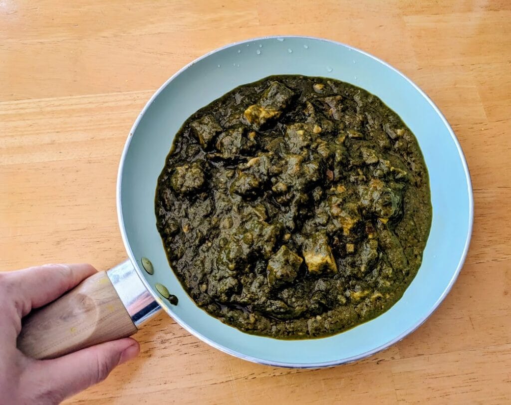 A hand holding a ceramic skilled filled with palak paneer from MTR Minute Meals.