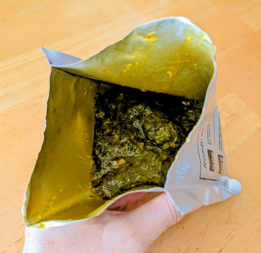 A hand holding an open foil pouch of palak paneer from MTR Minute Meals.