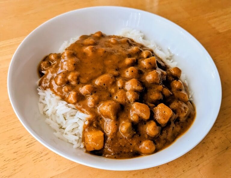 A white bowl with basmati rice topped with Maya Kaimal Organic Madras Potato Curry.