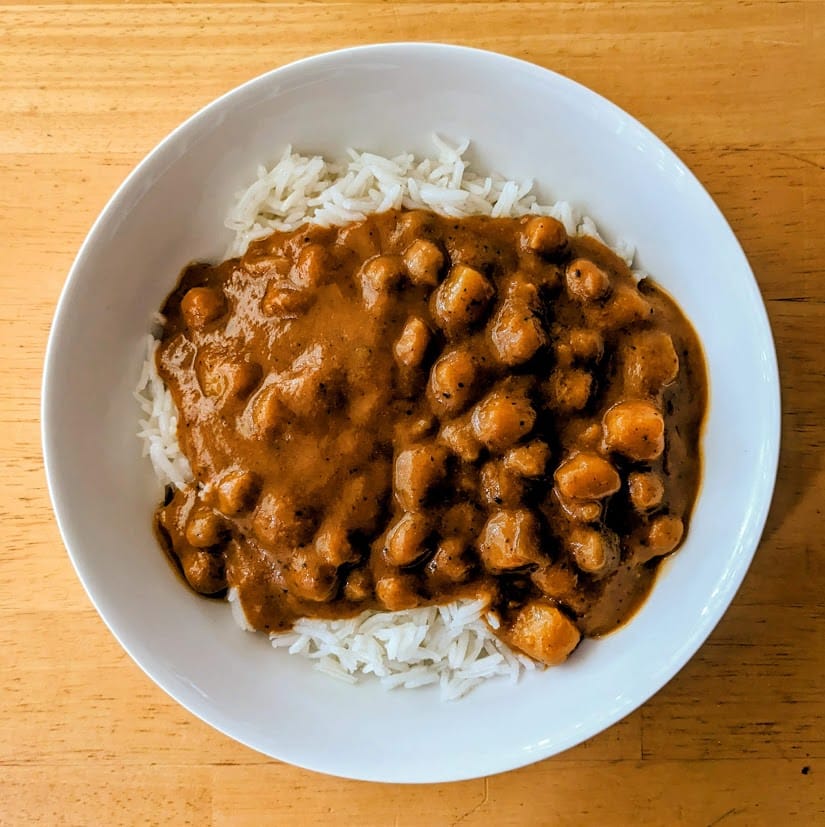 A white bowl with basmati rice and chickpeas in sauce from a Maya Kaimal Madras Potato Curry meal.