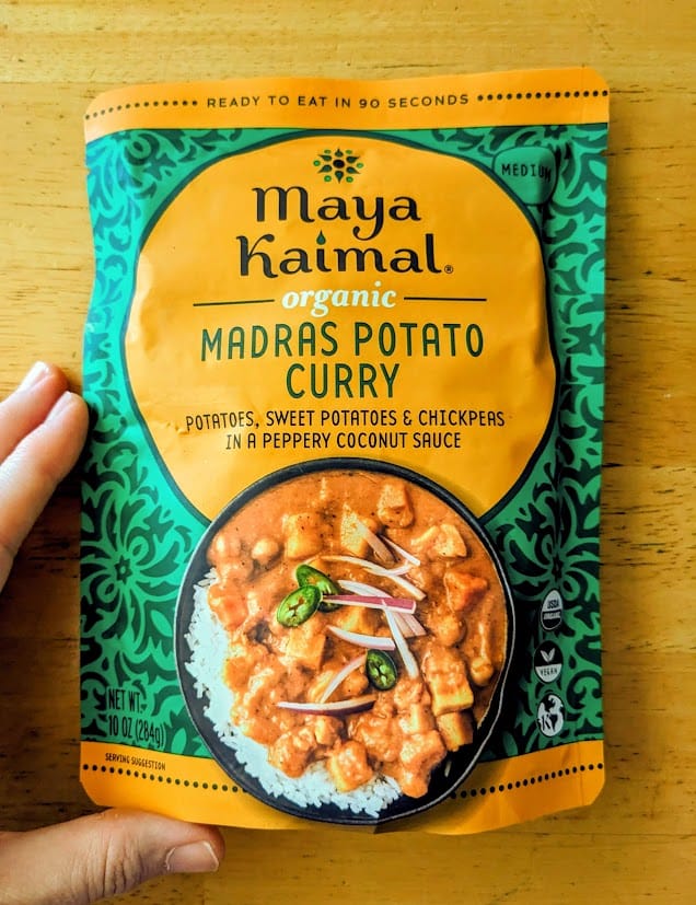 A hand holding a pouch of Maya Kaimal Organic Madras Potato Curry from Costco.