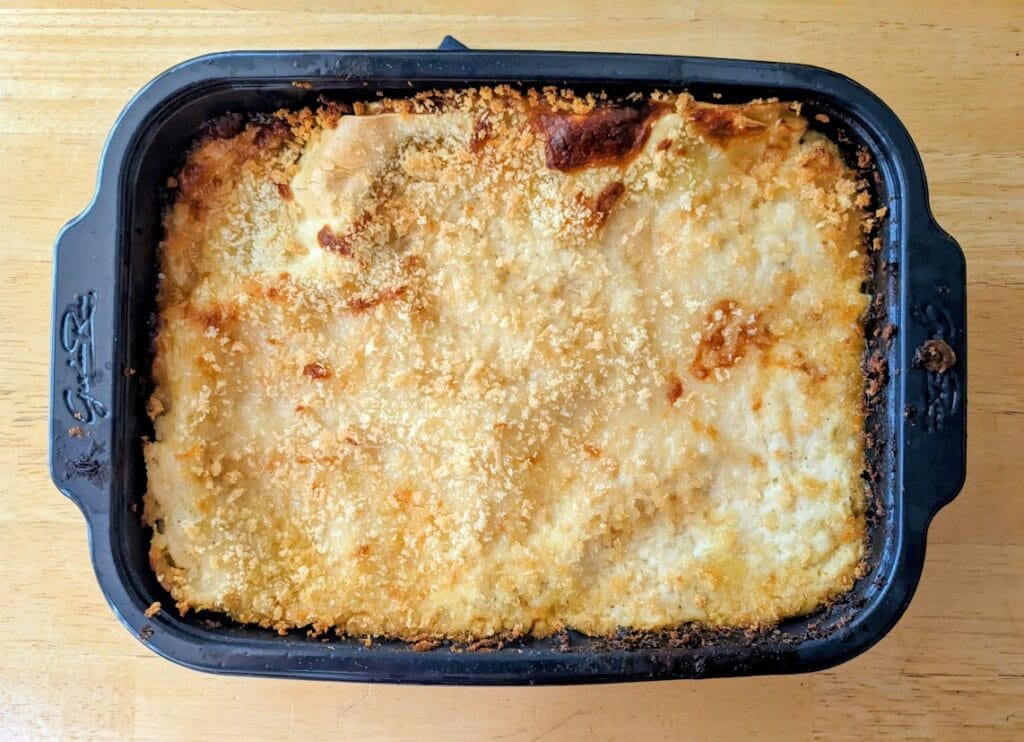 A plastic pan of baked Chicken Carbonara Lasagna from Rana sitting on a kitchen table.