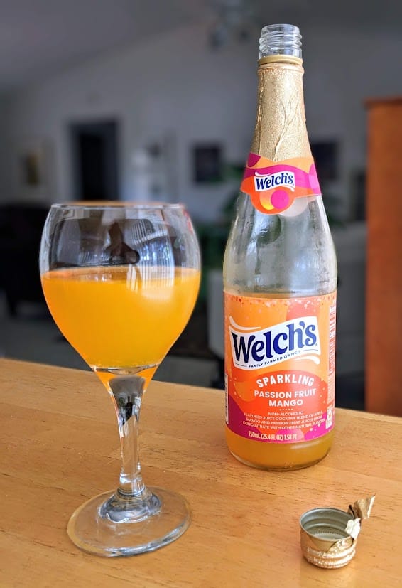 A goblet filled with Sparkling Passion Fruit Mango drink from Welch's, next to a bottle.