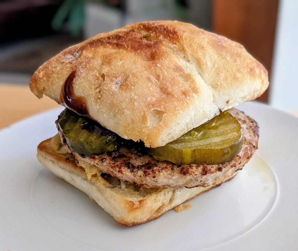 A turkey burger on a bun with Bubbies Bread & Butter Pickles.