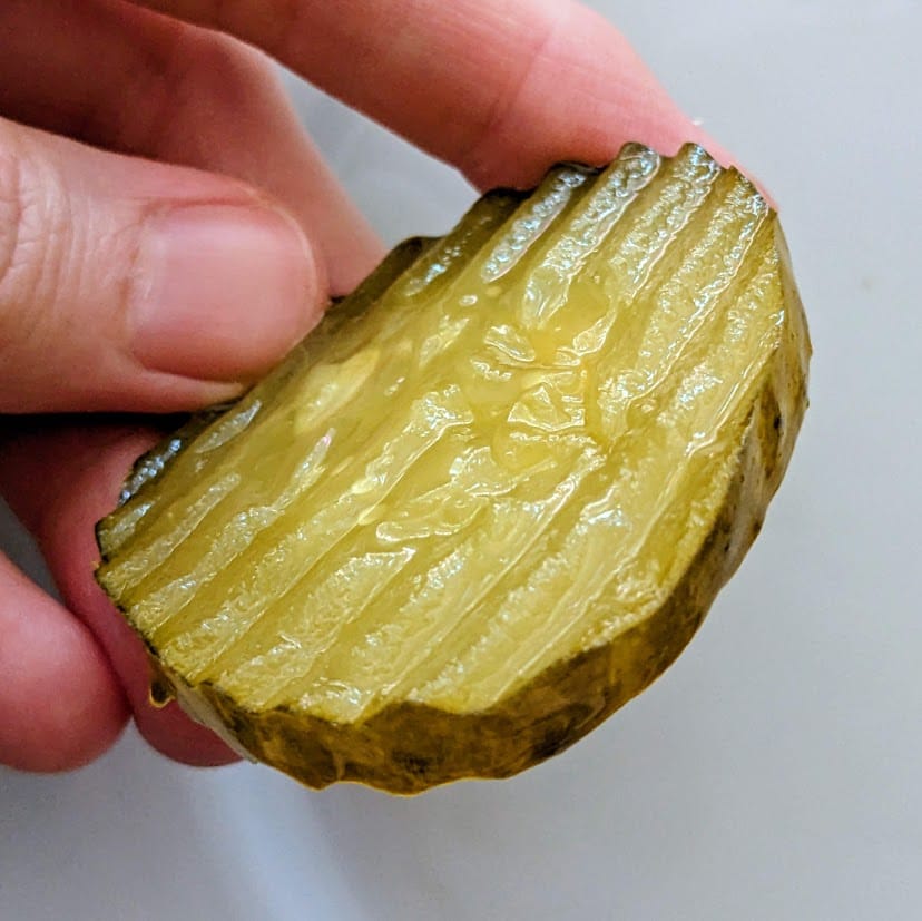 Fingers holding a large Bubbies Bread & Butter pickle chip.