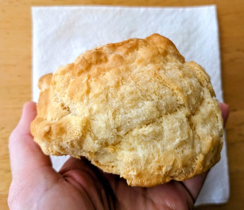 A hand holding the side of a whole Buttermilk Biscuit from the Costco Bakery.