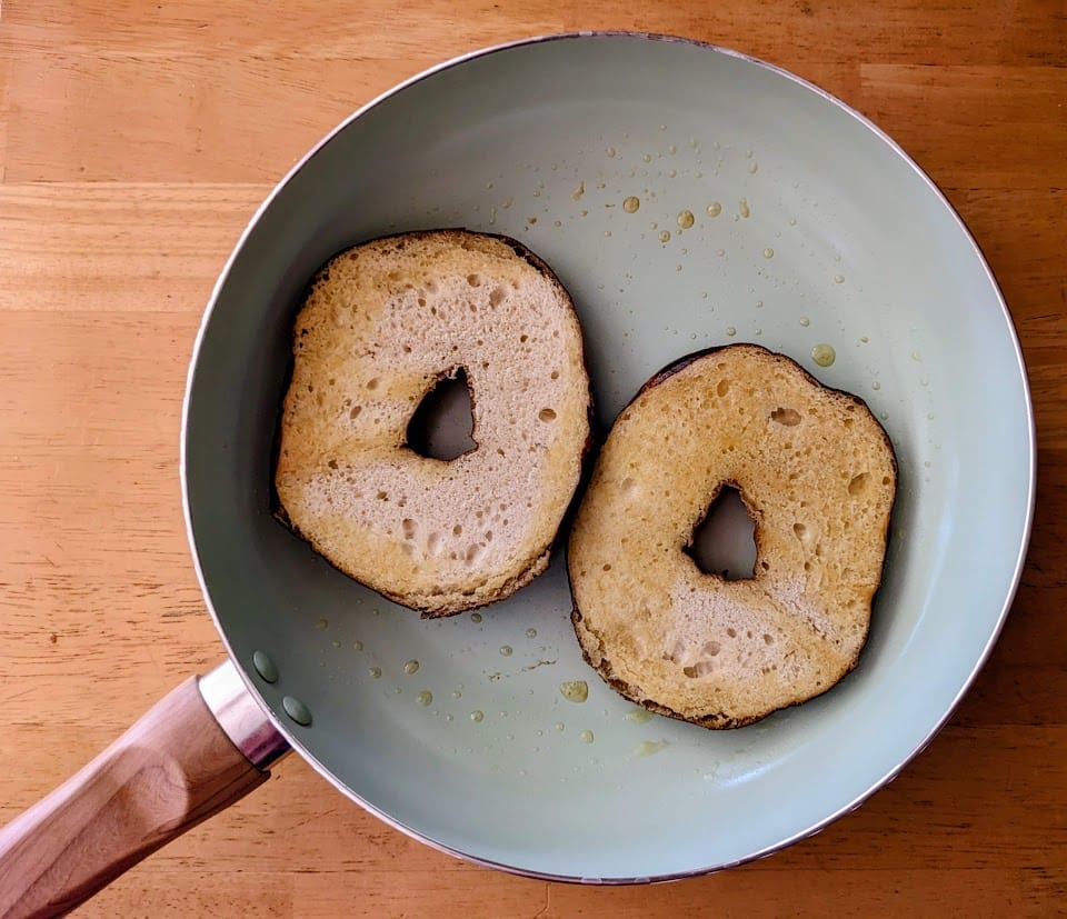 A ceramic pan with two buttered halves of a Costco Pretzel Bagel.