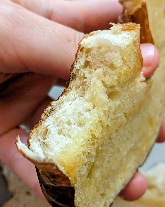A hand holding a bitten piece of buttered Pretzel Bagel from the Costco Bakery.