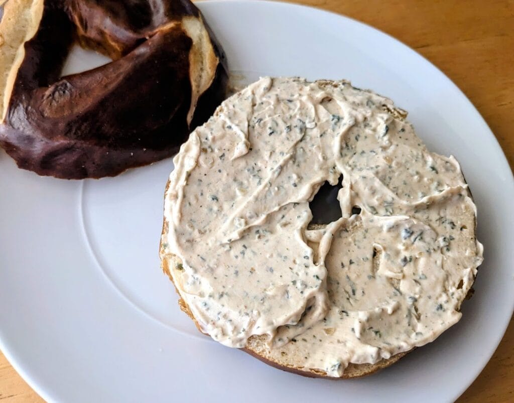 A Costco Pretzel Bagel covered in MyThreeSons Tuscan Sun Spread.