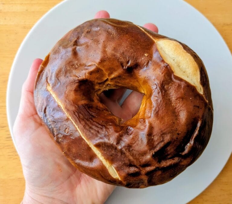 A hand holding a whole Costco Pretzel Bagel.
