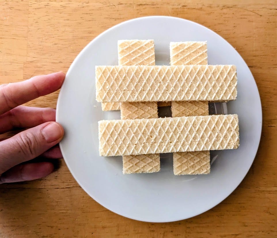 A hand holding a small white plate with stacked layers of Flora Italian Lemon Cream Wafer Cookies.