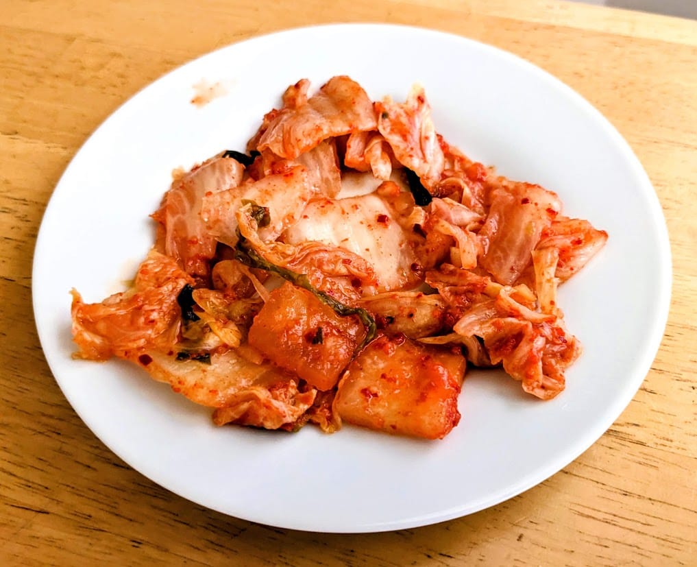 A small white plate with a pile of red Jongga Korean Kimchi.