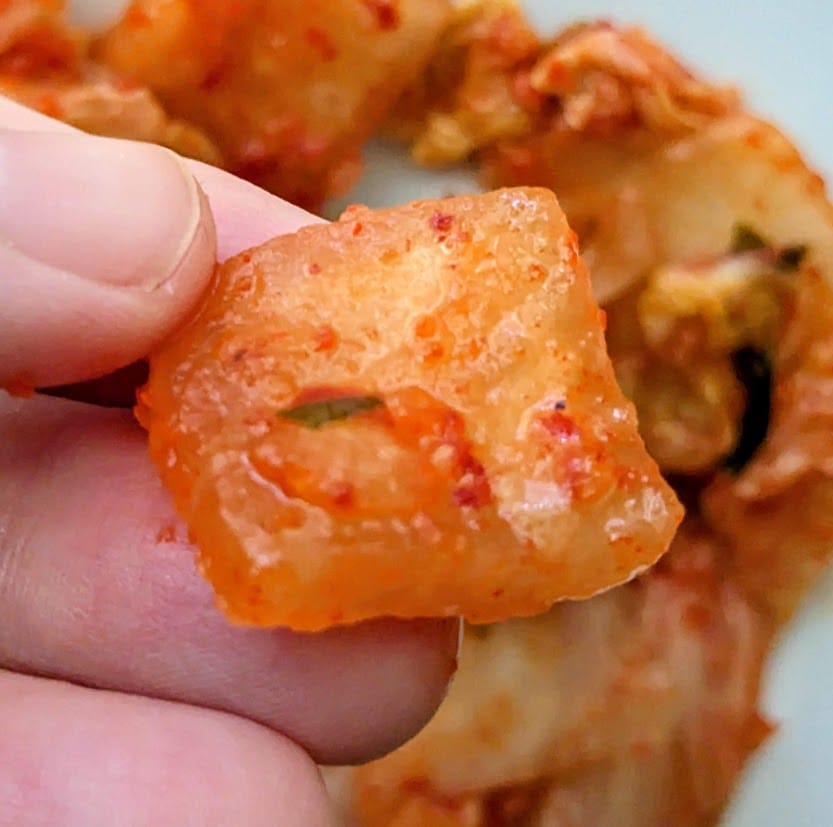 Fingers holding a square piece of radish from Jongga Korean Kimchi.