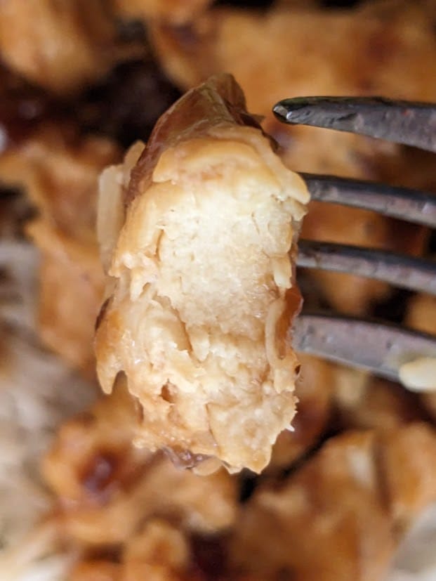 A fork holding a bite of meat from Kevin's Hawaiian-Style Chicken meal.
