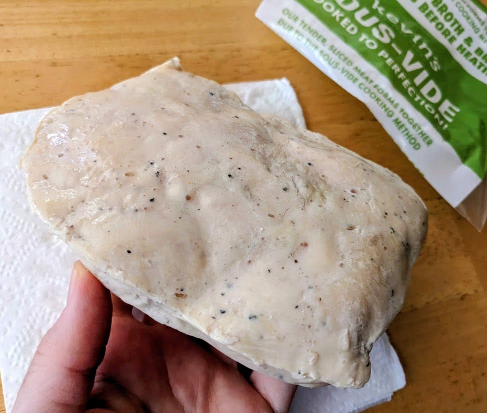 A hand holding a block of sous-vide meat from Kevin's Hawaiian-Style Chicken.