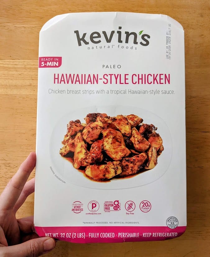 A hand holding a package of Kevin's Paleo Hawaiian-Style Chicken from Costco.