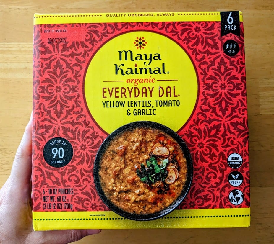 A hand holding a large box of Maya Kaimal Organic Everyday Dal from Costco.