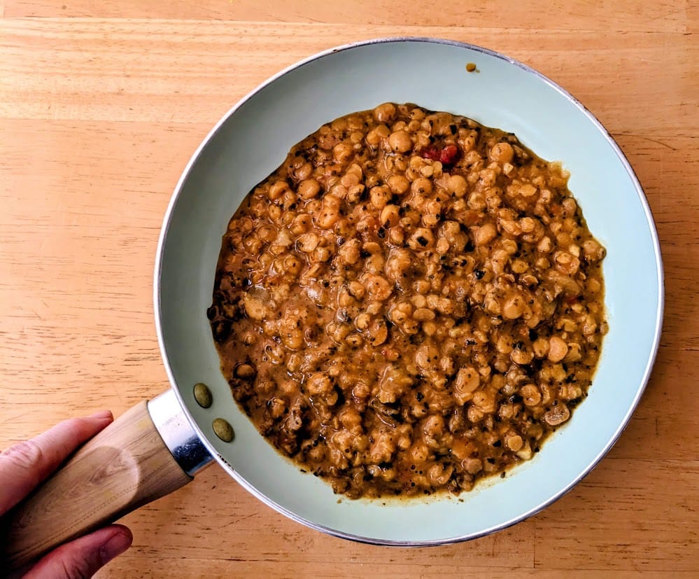 A hand holding a skillet filled with Maya Kaimal Indian Everyday Dal.
