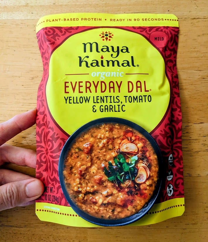 A hand holding a pouch of Maya Kaimal Organic Everyday Dal.