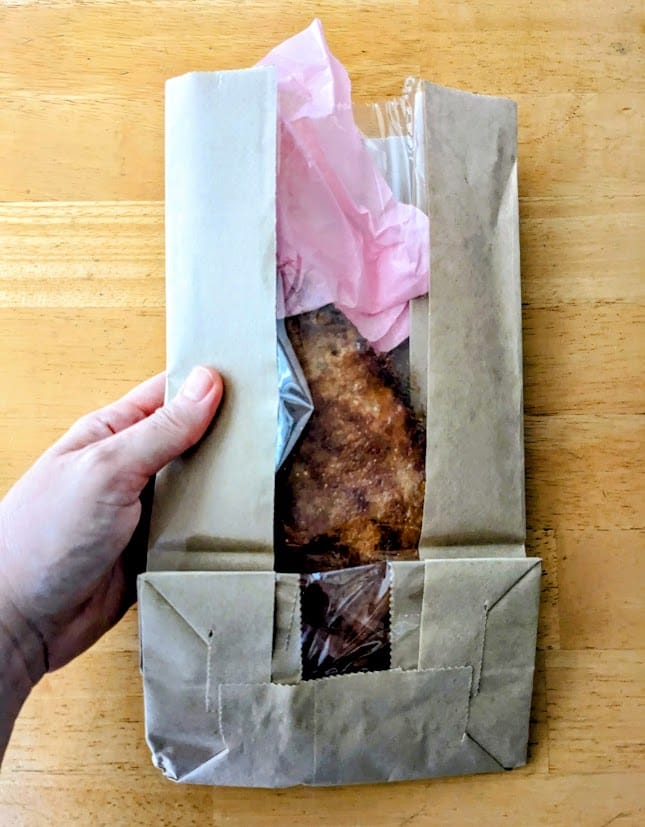 A hand holding a paper bag with an Apple Flip pastry from the Publix Bakery.
