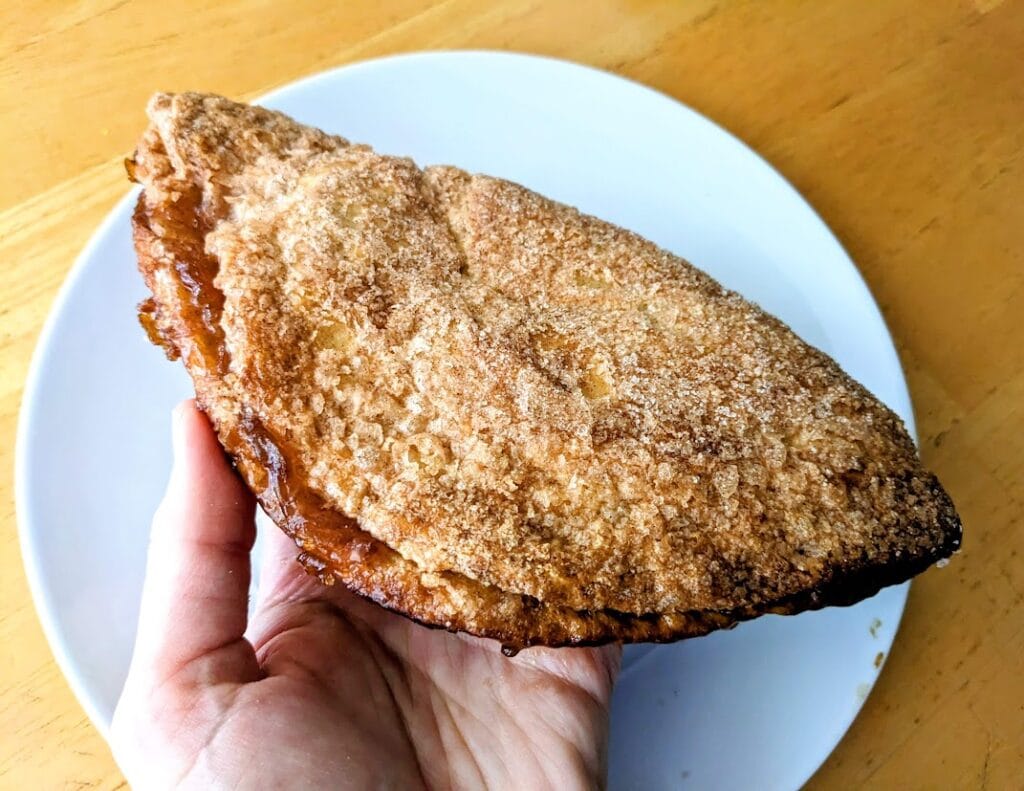 A hand holding a whole Publix Apple Flip pastry.